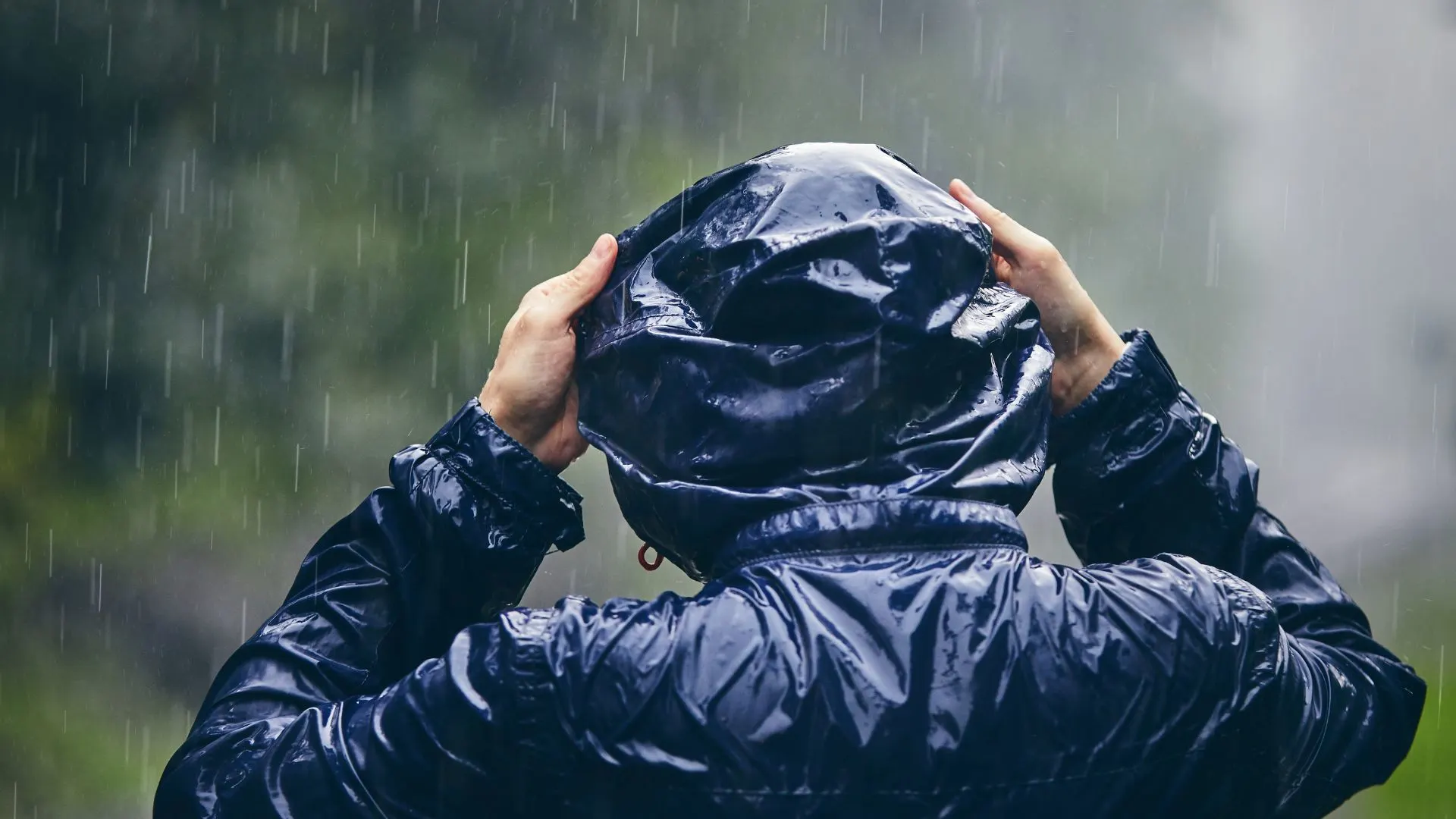 Person adjusting the hood of their raincoat in the rain.